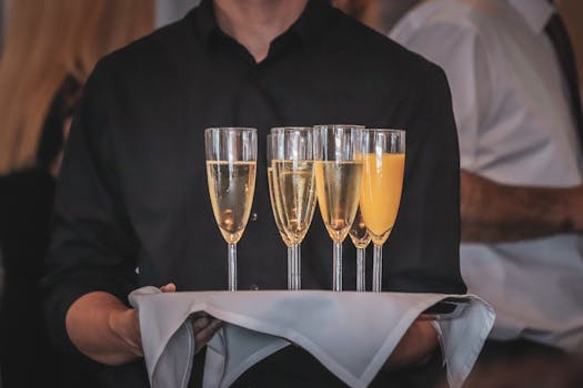 Close-up of a waiter holding a tray with champagne and orange juice glasses at an event.